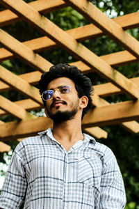 Young man wearing eyeglasses while standing against fence