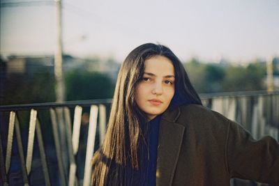 Portrait of young woman standing against railing