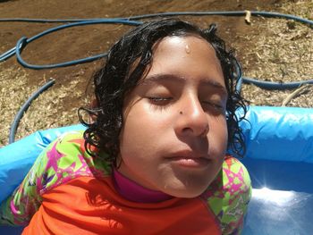 High angle close-up of boy with eyes closed sitting on wading pool during sunny day