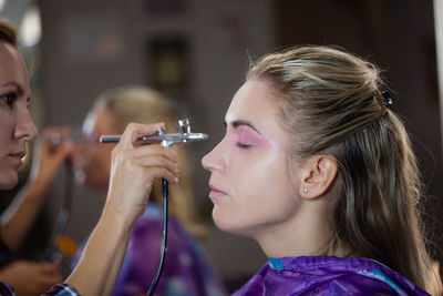 Female artist spraying makeup on eye of female model at studio