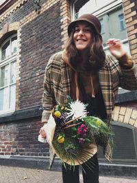 Portrait of young woman wearing hat standing against wall outdoors