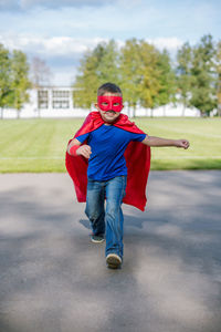 Full length of boy in superman costume walking on road against sky