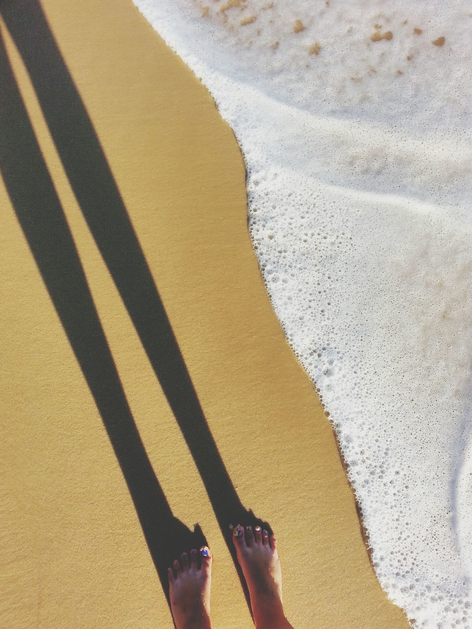 low section, person, lifestyles, leisure activity, high angle view, personal perspective, sand, beach, shadow, human foot, standing, sunlight, barefoot, men, unrecognizable person, day