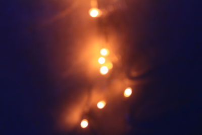 Defocused image of illuminated lights against sky at night