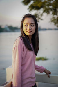 Portrait of young woman standing against lake