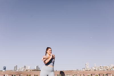 Woman standing by cityscape against clear sky