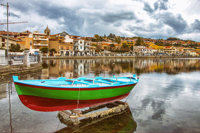 Boats moored in river by buildings in city against sky