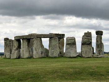 Stone structure on field against cloudy sky