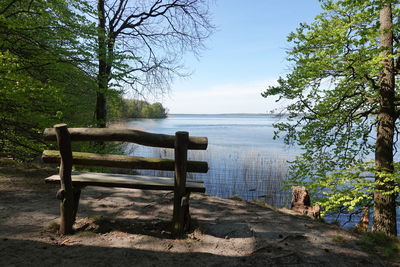 Empty park bench by sea against sky