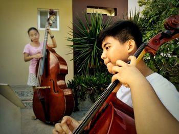 Siblings playing cello outside house