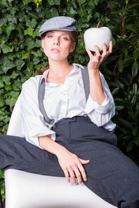 Portrait of woman wearing cap holding while apple at backyard