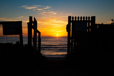 Silhouette wooden posts on beach against sky during sunset