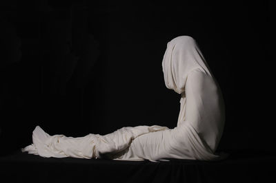 Person wrapped in fabric while sitting against black background