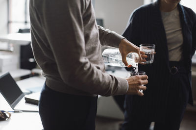 Midsection of businessman pouring water in drinking glass in office