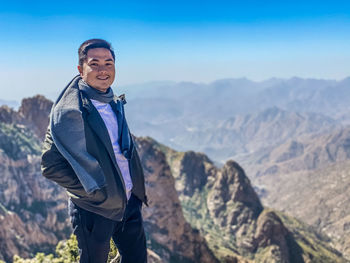 Smiling young man standing against mountain and sky