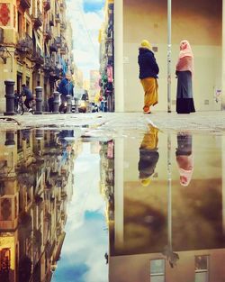Rear view of people walking by buildings in city