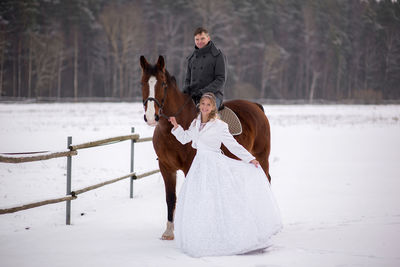 Portrait of smiling bride and groom with horse on snow covered field