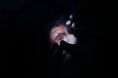 Midsection of man holding eyeglasses against black background