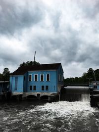 Building by river against cloudy sky