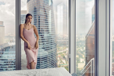 Woman in a nightgown stands at the window in a skyscraper near the bed