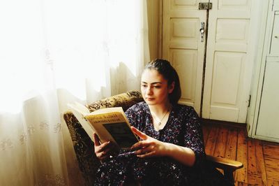 Beautiful young woman sitting on book at home