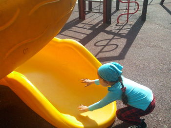 High angle view of girl crouching by yellow slide at playground