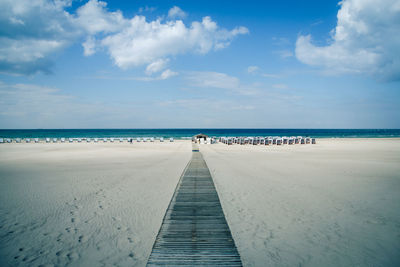 Boardwalk leading towards sea against sky