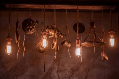 Low angle view of illuminated light bulb and antique hanging in darkroom