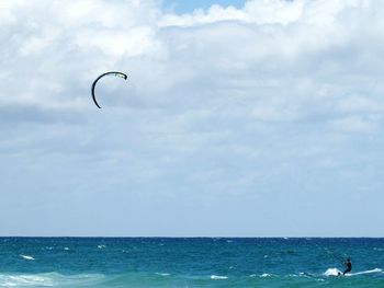 Person kiteboarding in sea against cloudy sky