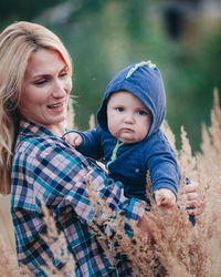 A young mother walks with her baby in a field with tall grass.