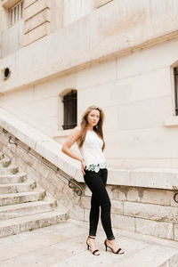 Full length portrait of young woman standing against building