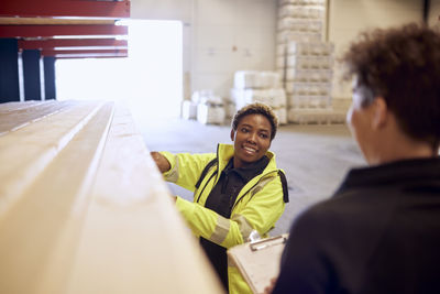 Smiling female worker discussing with colleague while working in lumber industry