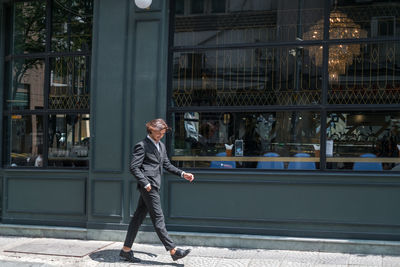 Successful stylish man in formal black suit walking on the street near dark-green wall. high quality 