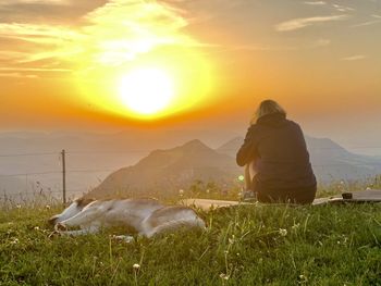 Rear view of woman by dog on mountain during sunset