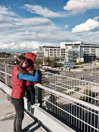 Full length of boy standing by railing in city against sky