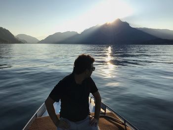 Man sitting on shore by sea against sky