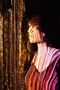 Portrait of woman standing against illuminated light painting at night