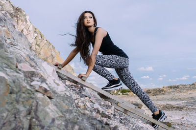 Low angle view of young woman climbing on rock