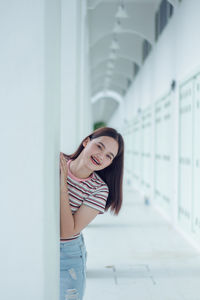 Portrait of smiling young woman standing against white wall