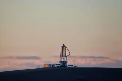 Communications tower on field against sky at sunset