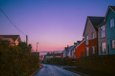 Empty road amidst houses and buildings against sky during sunset