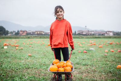 Girl in orange hoodie with pumkins standing on a field