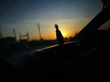 Close-up of silhouette bird on car against sky during sunset
