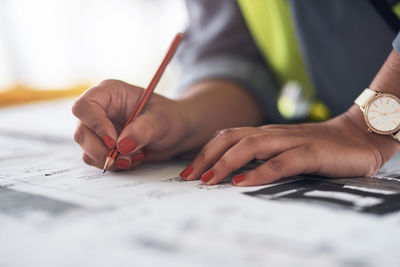 Midsection of architect drawing blueprint on table