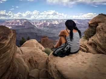 Rear view of woman sitting on rock against mountains