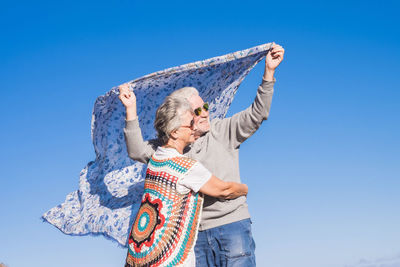 Senior couple holding scarf against clear blue sky