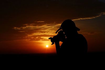 Silhouette man photographing against sky during sunset