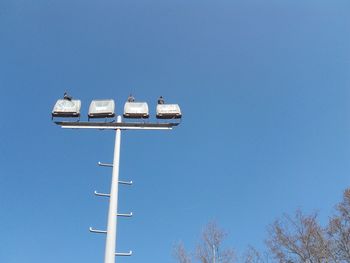 Low angle view of birds perching on floodlight against sky