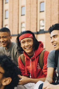 Portrait of cheerful young man sitting by friends in city