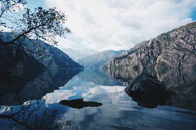 Scenic view of lake sary-chelek by mountains against cloudy sky